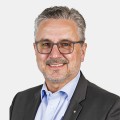 Ein Verkaufsmitarbeiter der Firma Ebnat AG im mittleren Alter l&auml;chelt. Er tr&auml;gt eine graue Brille und hat ein blaues Hemd mit einem schwarze Blazer an. Seine Haare sind grau/weiss. Er hat einen kurzen und weissen Bart.